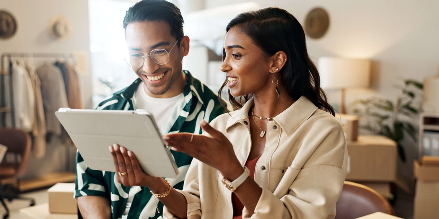 Zwei Menschen gucken lachend auf ein Tablet, die eine Person zeigt drauf.